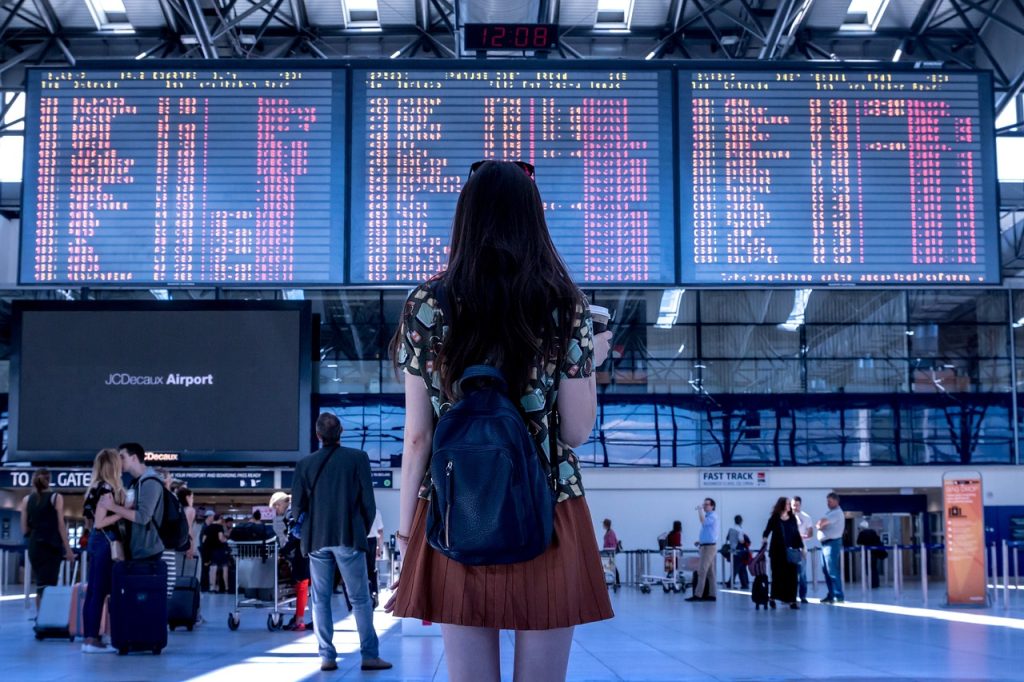 rimborso volo in ritardo, ragazza che guarda il tabellone in aeroporto, punto di rotta